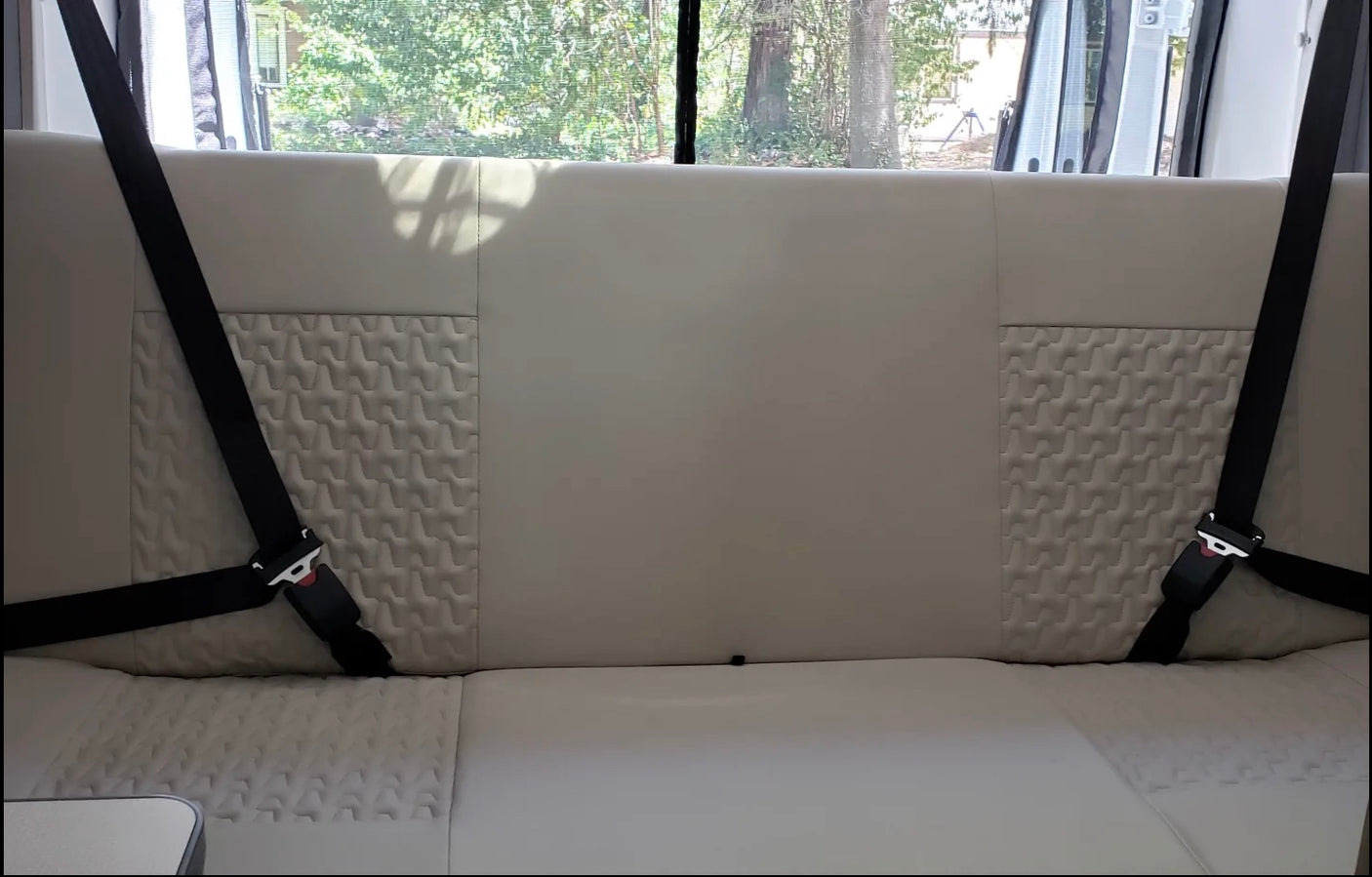 An RV rental's rear interior features a light bench seat, textured back panels, and two visible safety seatbelts.