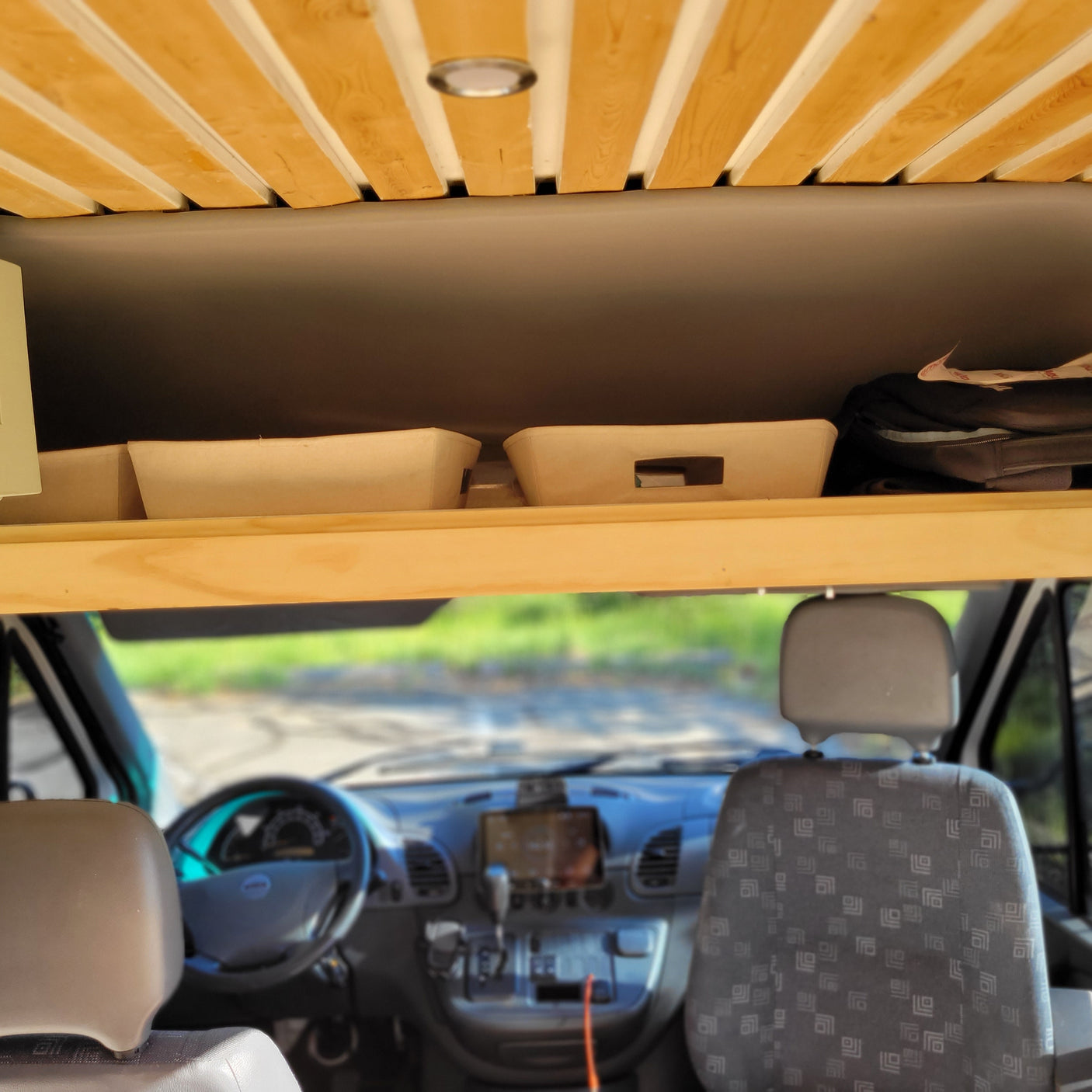 Inside an RV rental: Wooden slat ceiling, overhead storage, and view towards the front cabin with seats and dashboard.