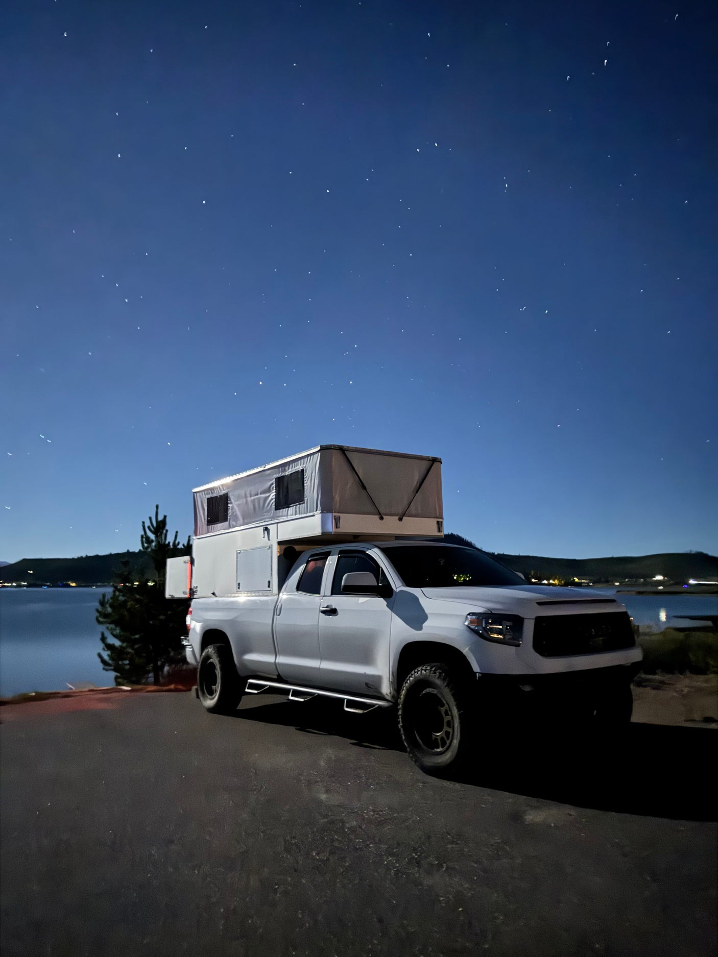 Stargazing from an RV rental: a white truck with a pop-up camper by a lake at night. Perfect for outdoor adventure & camping.
