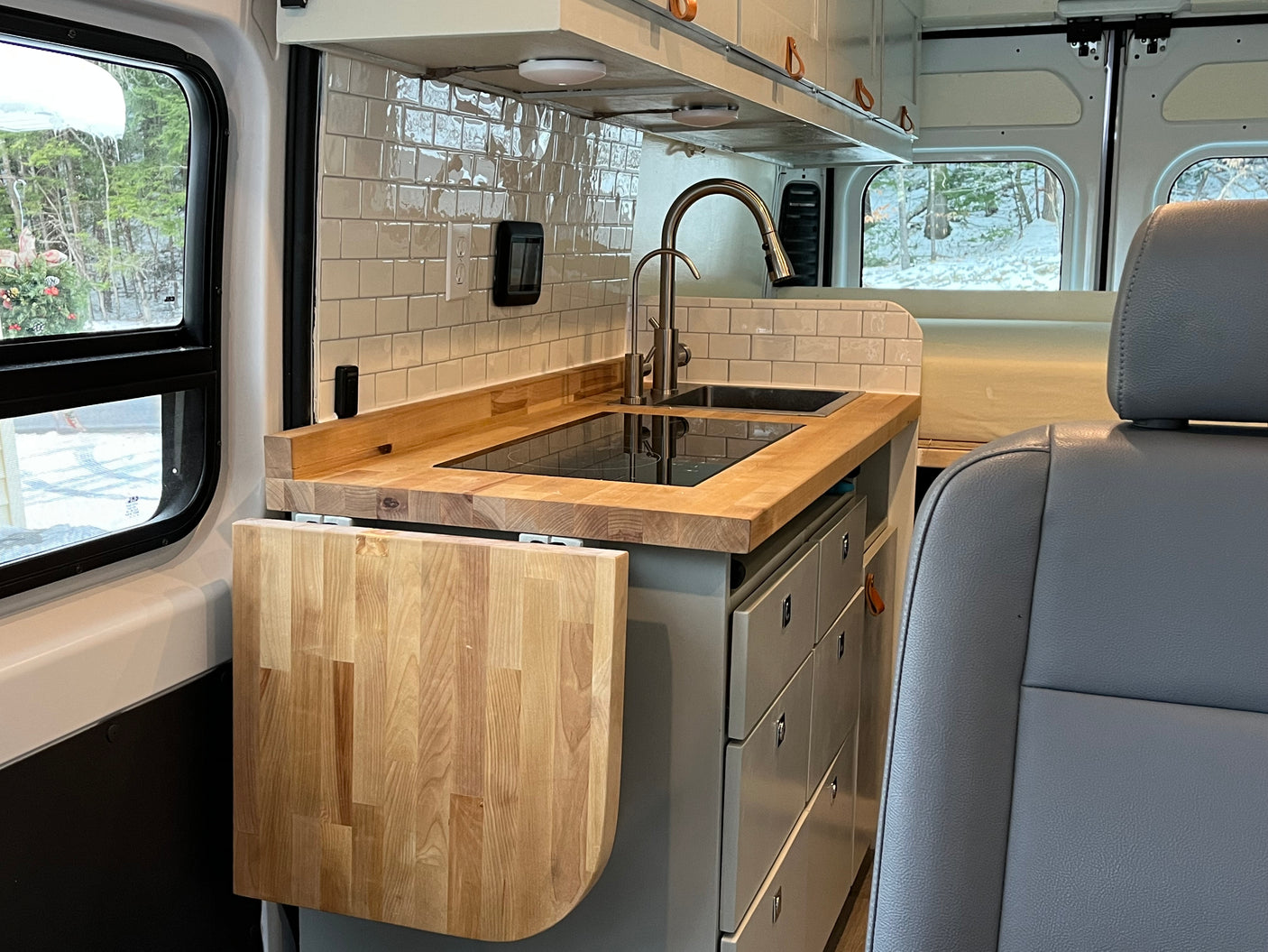 Compact RV rental kitchen with butcher block countertop, sink, cooktop, and fold-down table. Enjoy winter views!