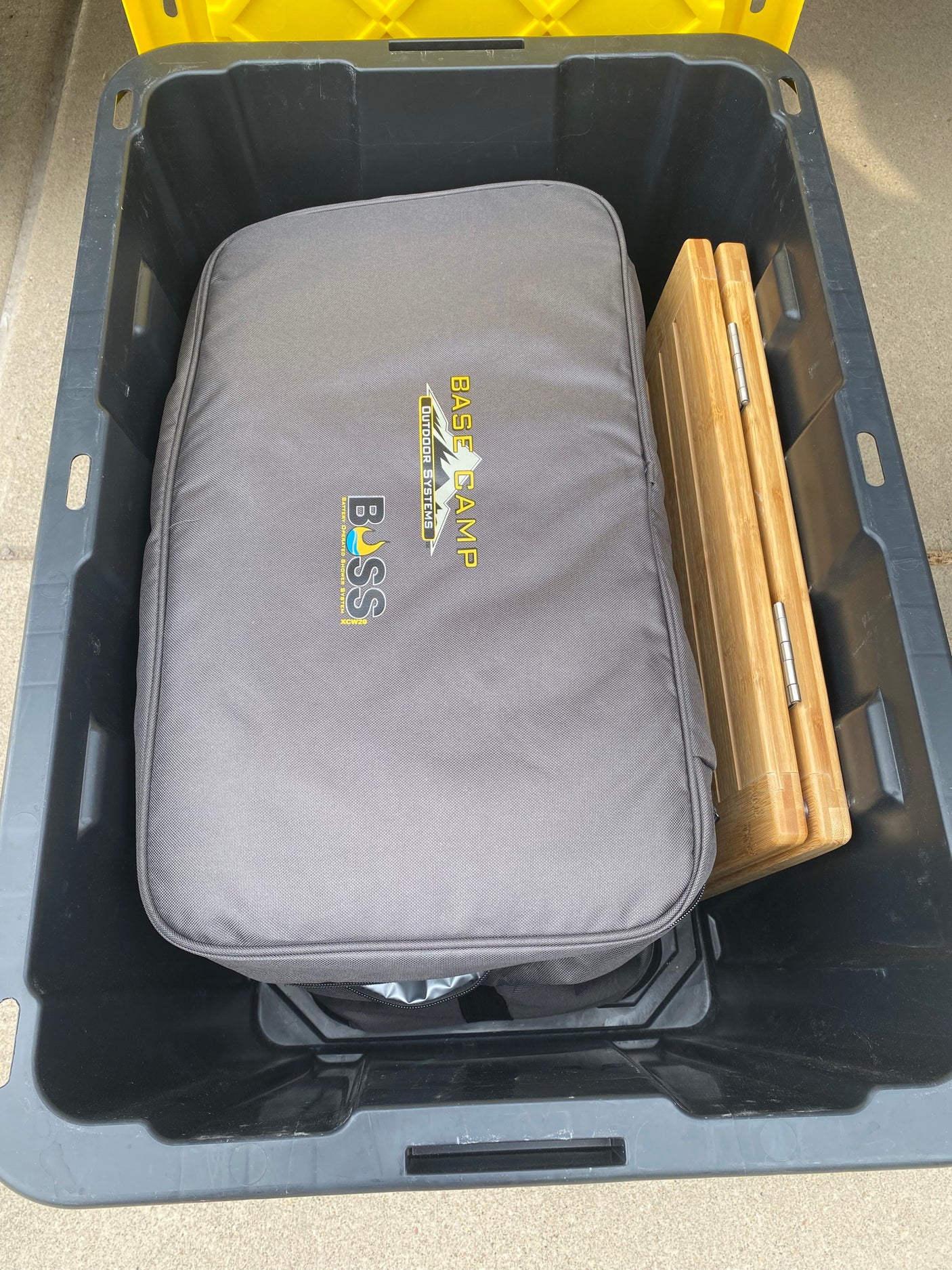 RV rental gear: a grey BOSS Base Camp carrying case and a folded bamboo item neatly stored in a black bin.