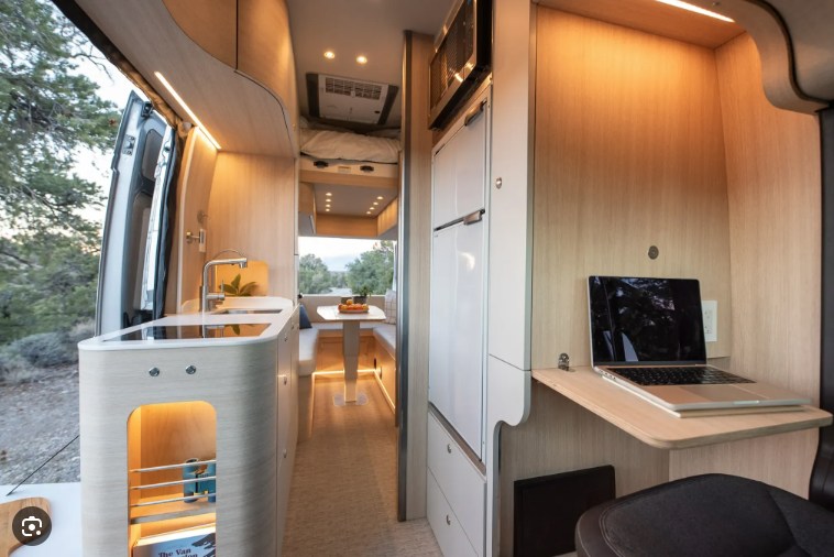Spacious RV rental interior featuring a modern kitchen, dining area, overhead bed, and a laptop on a dedicated workspace.