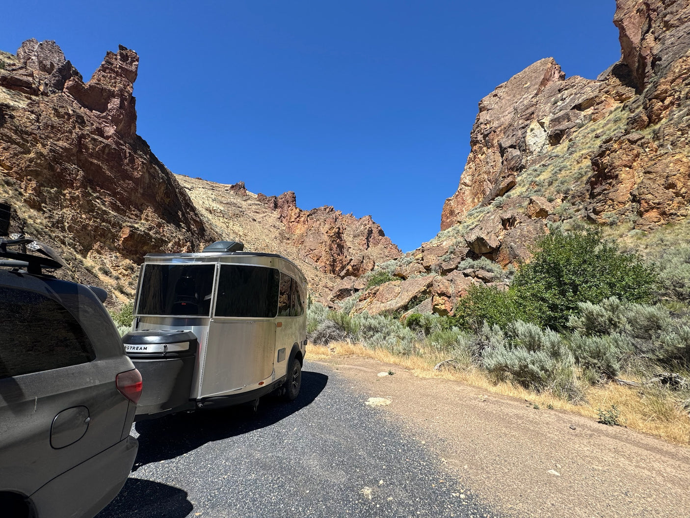 An Airstream rv rental and SUV parked in a dramatic canyon, surrounded by towering rock formations and clear blue sky.