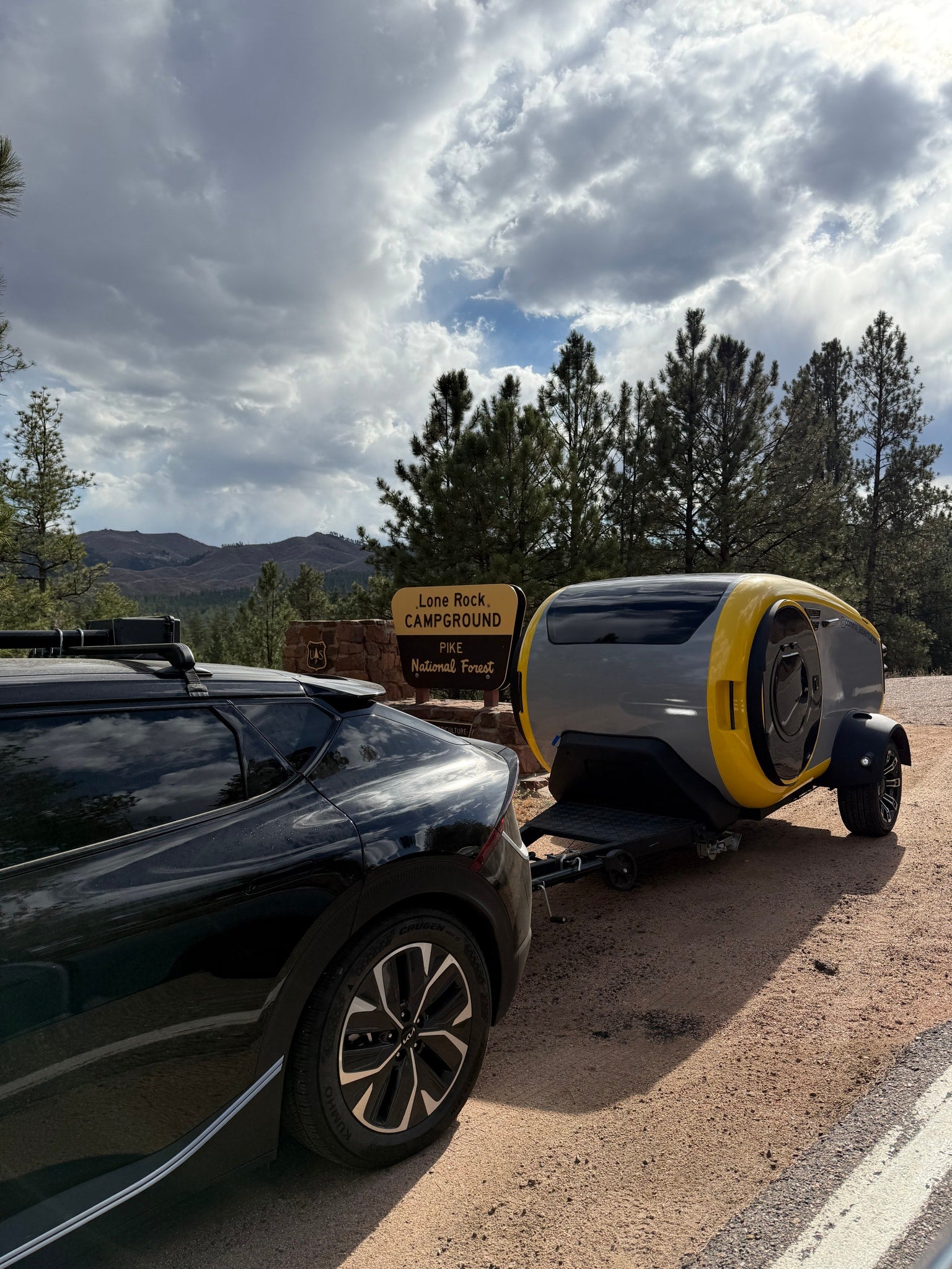 Modern Cortes RV rental for adventure at Lone Rock Campground, Pike National Forest, towed by a black car.