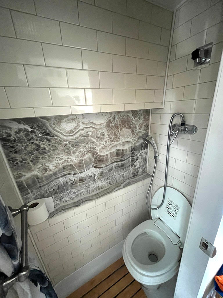 RV rental compact bathroom with toilet & handheld shower. Features white subway tiles & a striking grey/white stone niche.