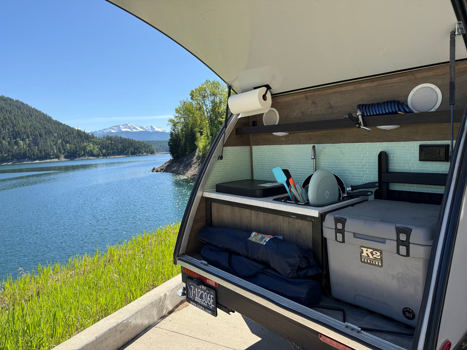 Enjoy the views! This RV rental features a convenient outdoor kitchen setup by a serene lake with mountains.
