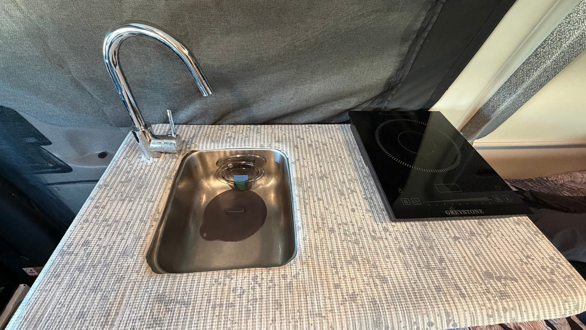 and front seats.|Rear of a white rv rental van with open door revealing a black privacy screen. Spare tire on left door. Tree reflections in window.|RV rental van's rear doors open — photo 16
