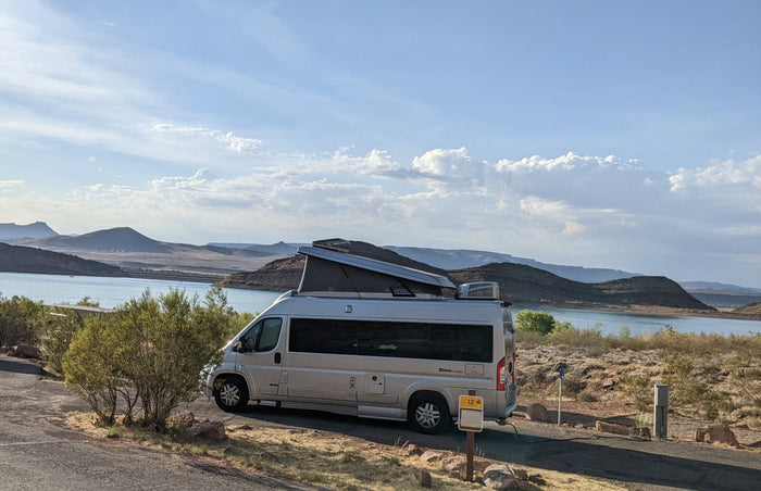 Enjoying a scenic lake view from an RV rental parked at a campsite, featuring a pop-top RV with mountains in the distance.