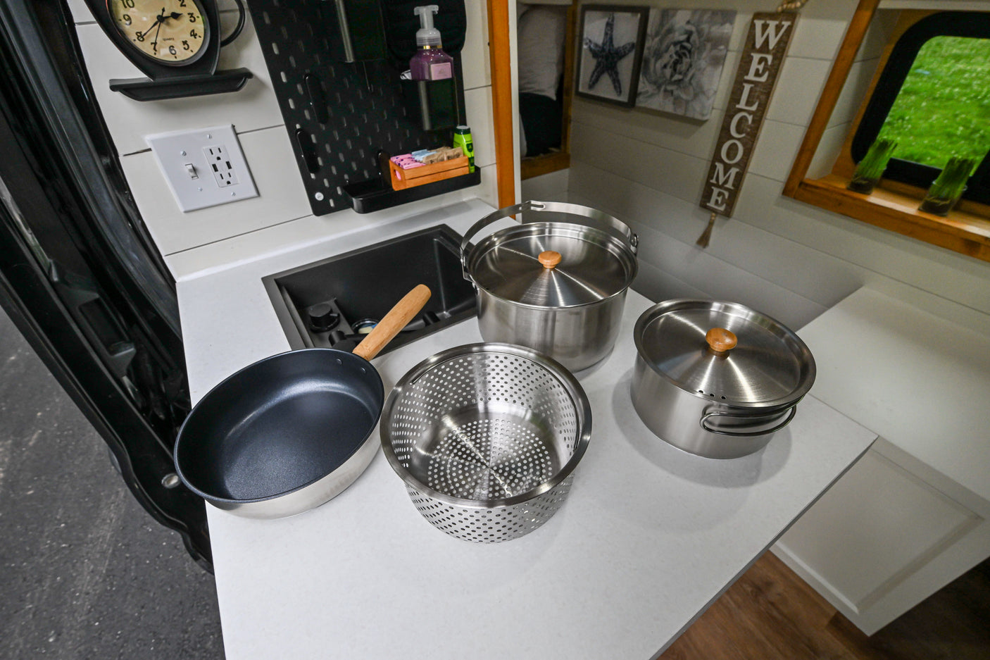 Compact RV rental kitchen counter with sink, various pots, pans, and a pegboard organizer for easy meal prep.