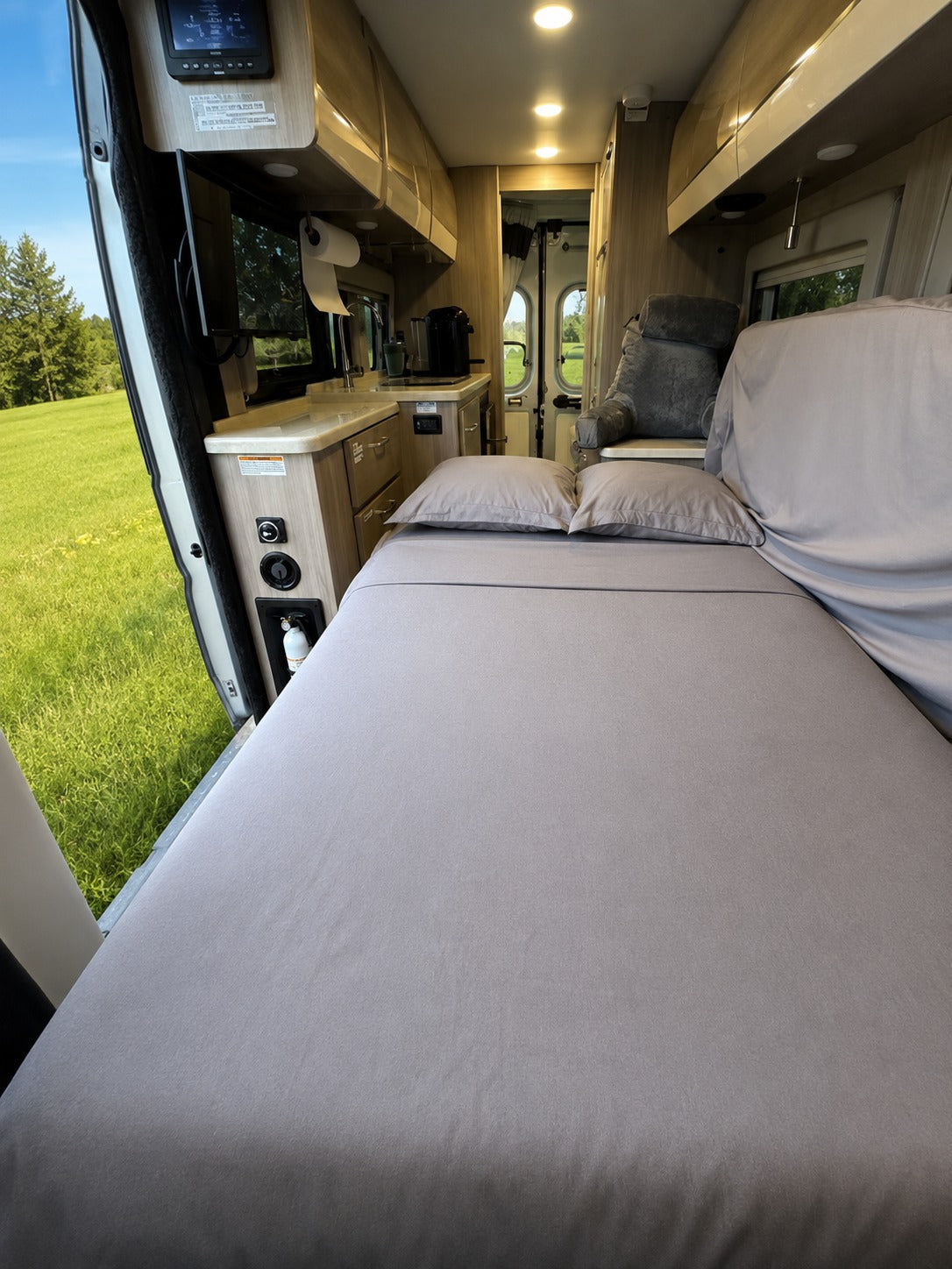 Cozy rv rental interior with a comfortable bed, compact kitchen, and a beautiful view of nature outside the door.