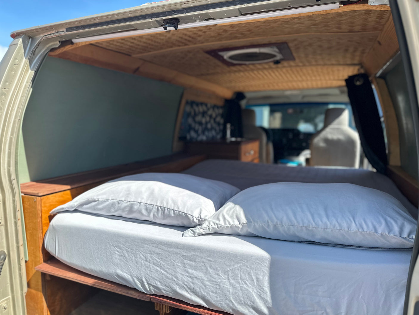 Cozy camper van interior of an RV rental with a comfortable bed, wooden walls, and roof fan, ready for adventure.