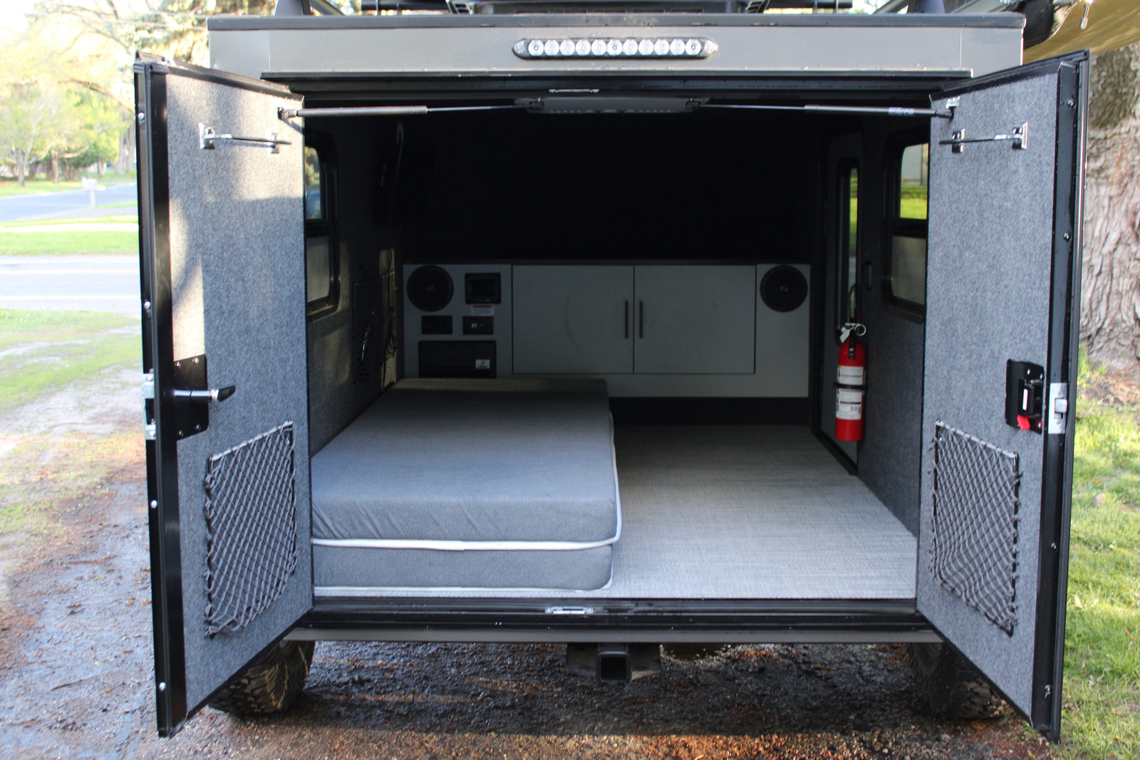 RV rental: view inside a compact camper with a bed, storage nets, controls, and a fire extinguisher ready for your adventure.