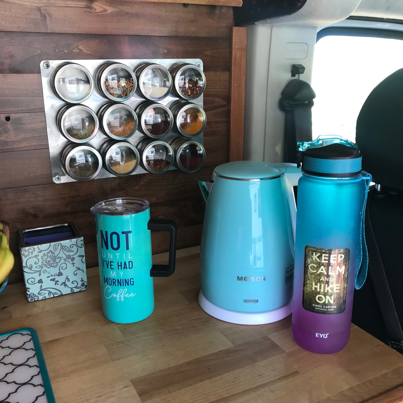 RV rental: a vibrant collection of travel essentials – kettle, water bottle, coffee mug, and magnetic spices on wood.