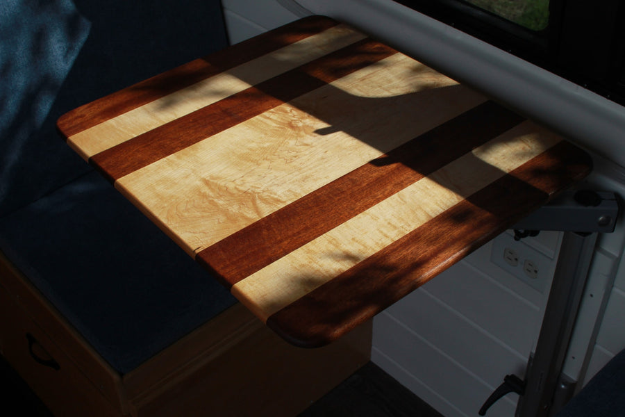 Striped wood table, illuminated by sun and shadows, in an RV rental. Note comfy seating & wall outlets for a versatile space.