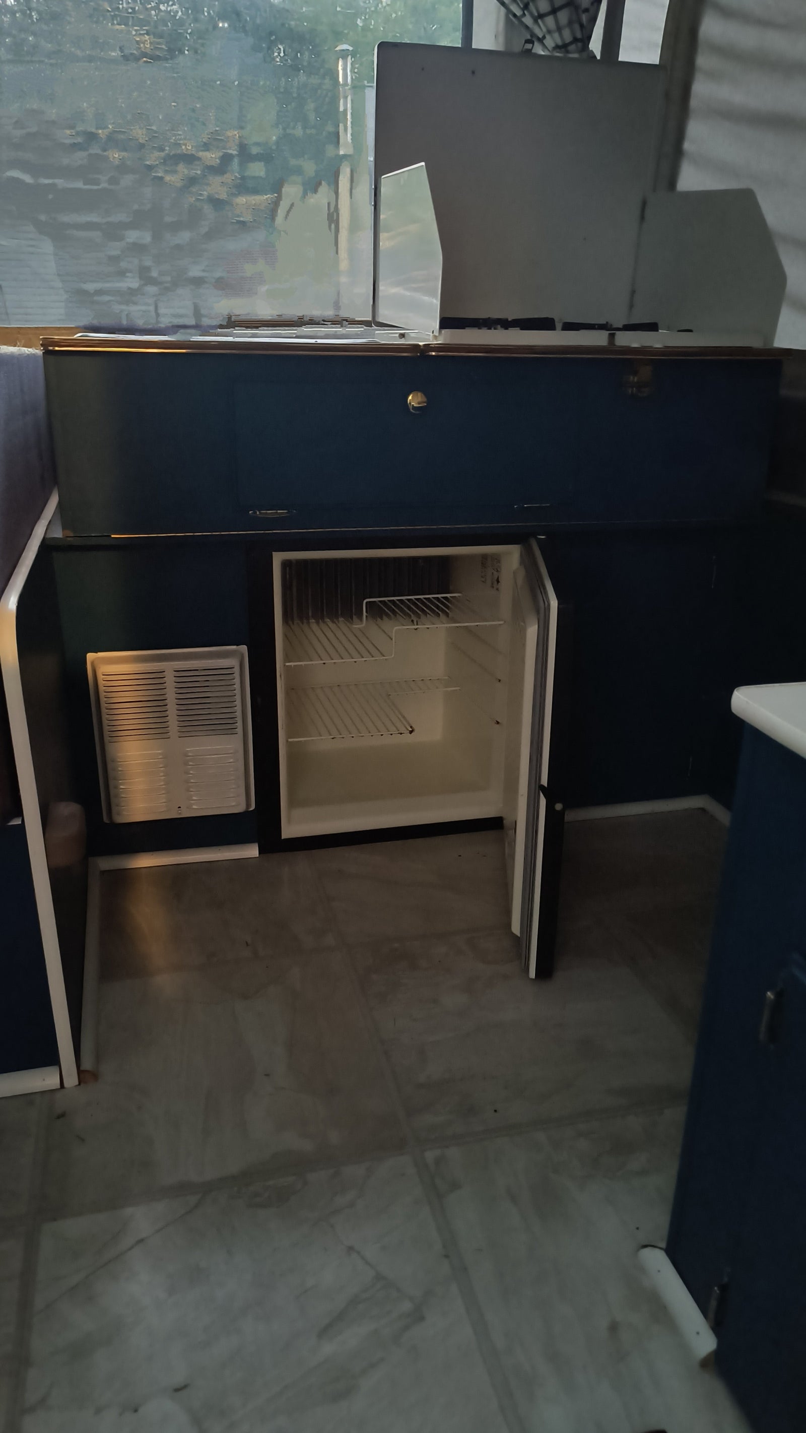 Inside this RV rental: A compact kitchen area featuring a top-mounted stove, open mini-fridge, and vent unit.