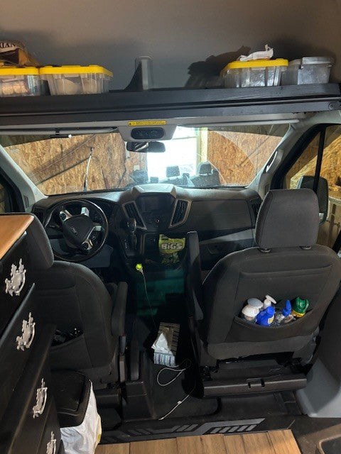 RV rental interior: Front cabin of a Ford Transit van with driver/passenger seats, dash, and overhead storage.