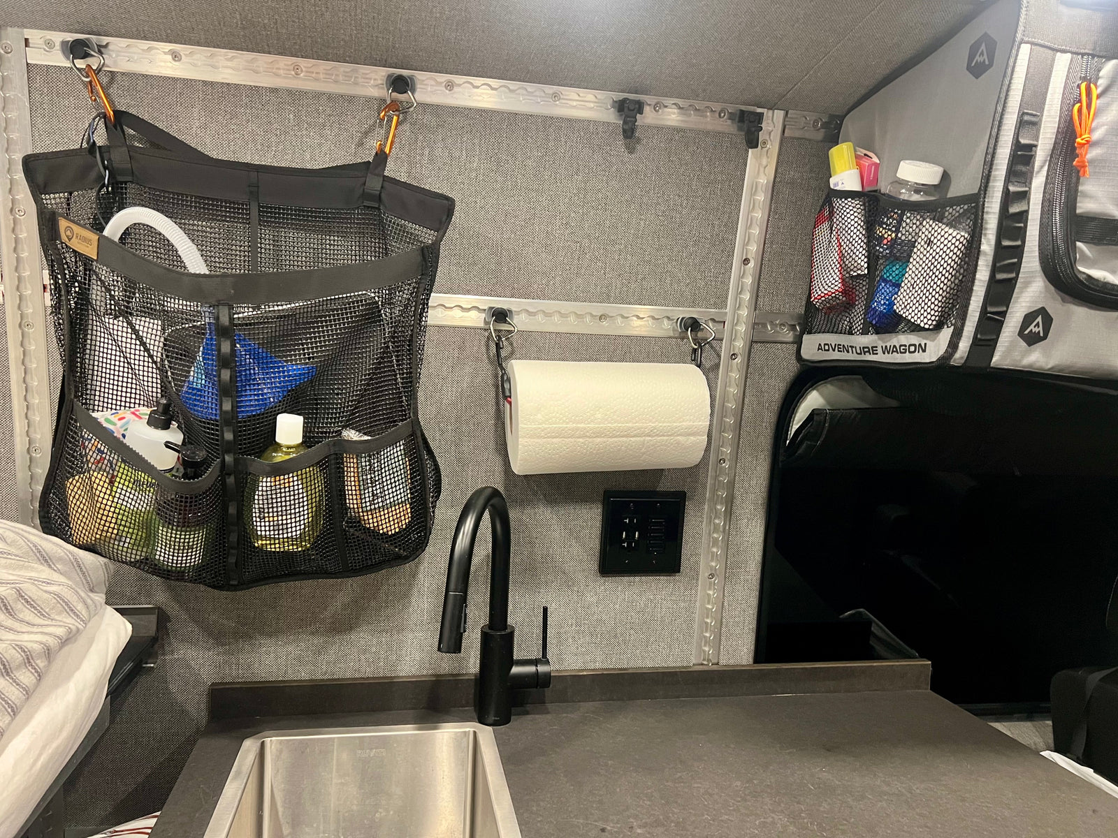 RV rental interior: sink, black faucet, mesh organizers, and charging station against gray walls for compact living.