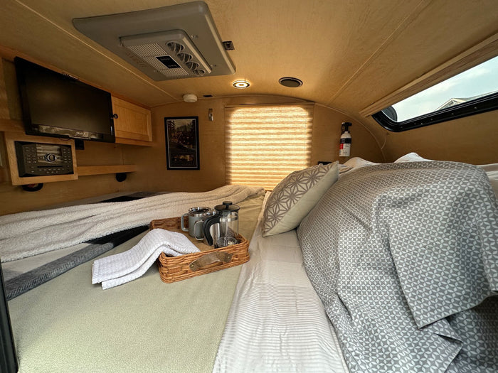 parked in a sunny green forest campsite. Ready for outdoor adventures.|Inside a cozy RV rental: comfy bed