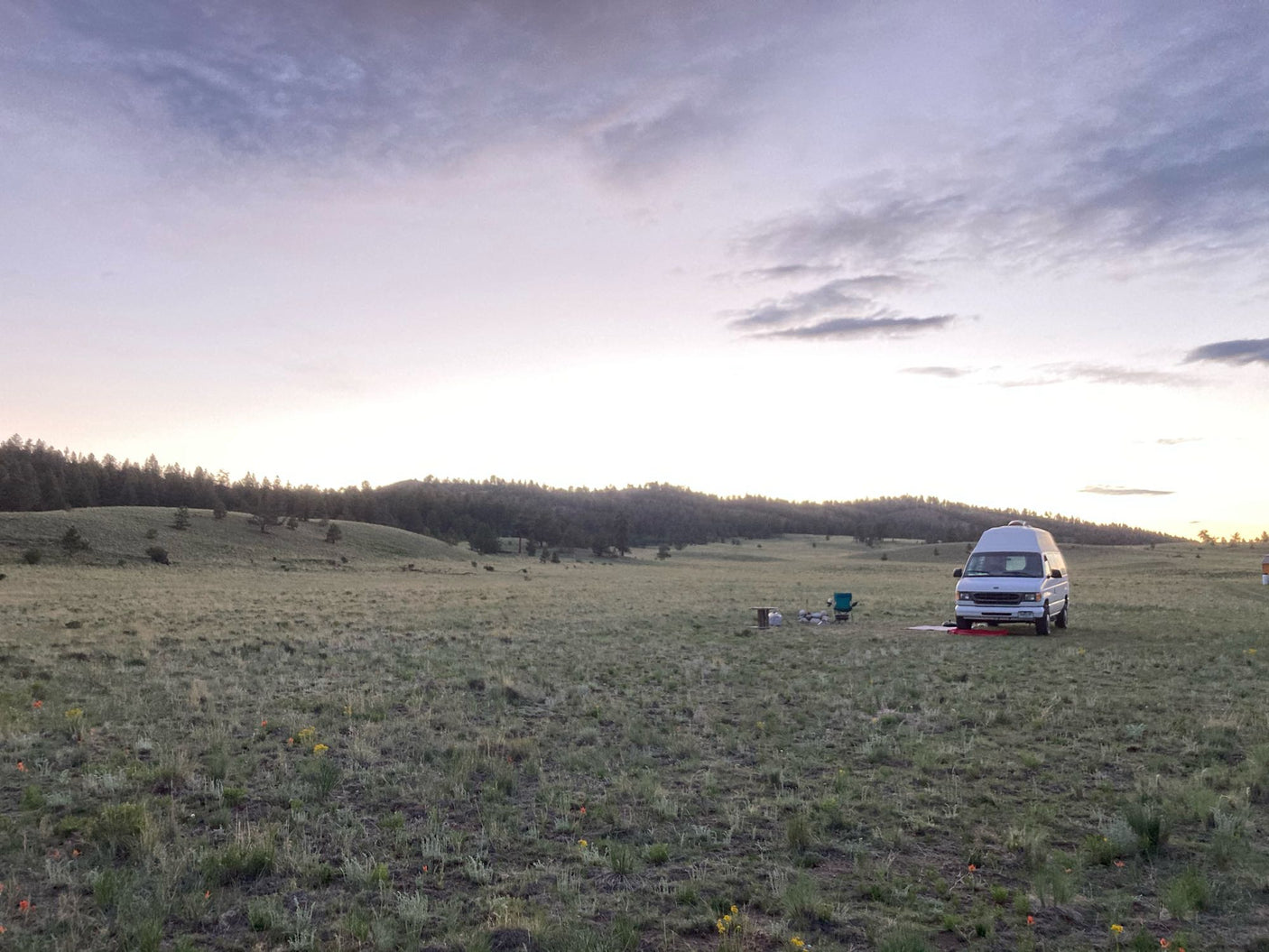 An RV rental parked in a vast grassy field with distant wooded hills, offering a serene outdoor camping experience.