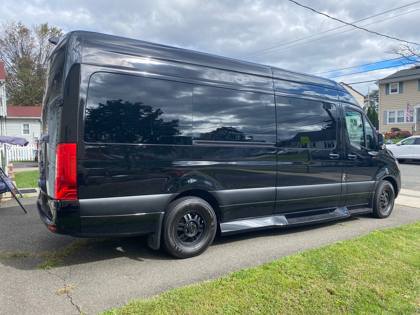 Sleek black RV rental van, a large Mercedes-Benz Sprinter, parked on asphalt, showcasing tinted windows.