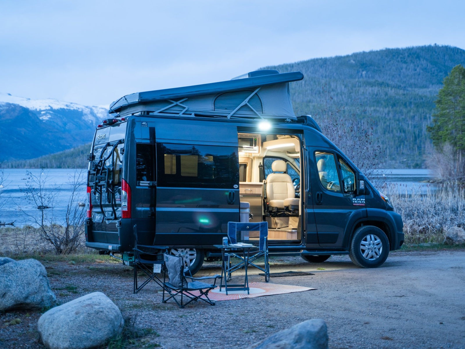 An rv rental camper van illuminates a lakeside campsite at dusk