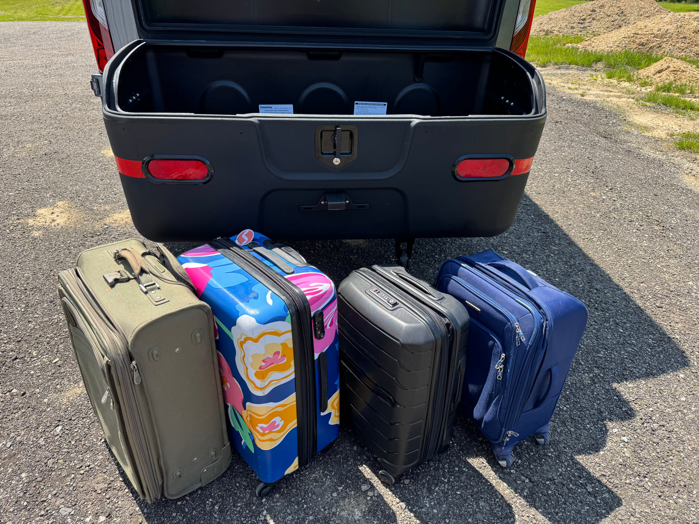Four suitcases ready for an RV rental trip, next to an open vehicle cargo box for extra storage.