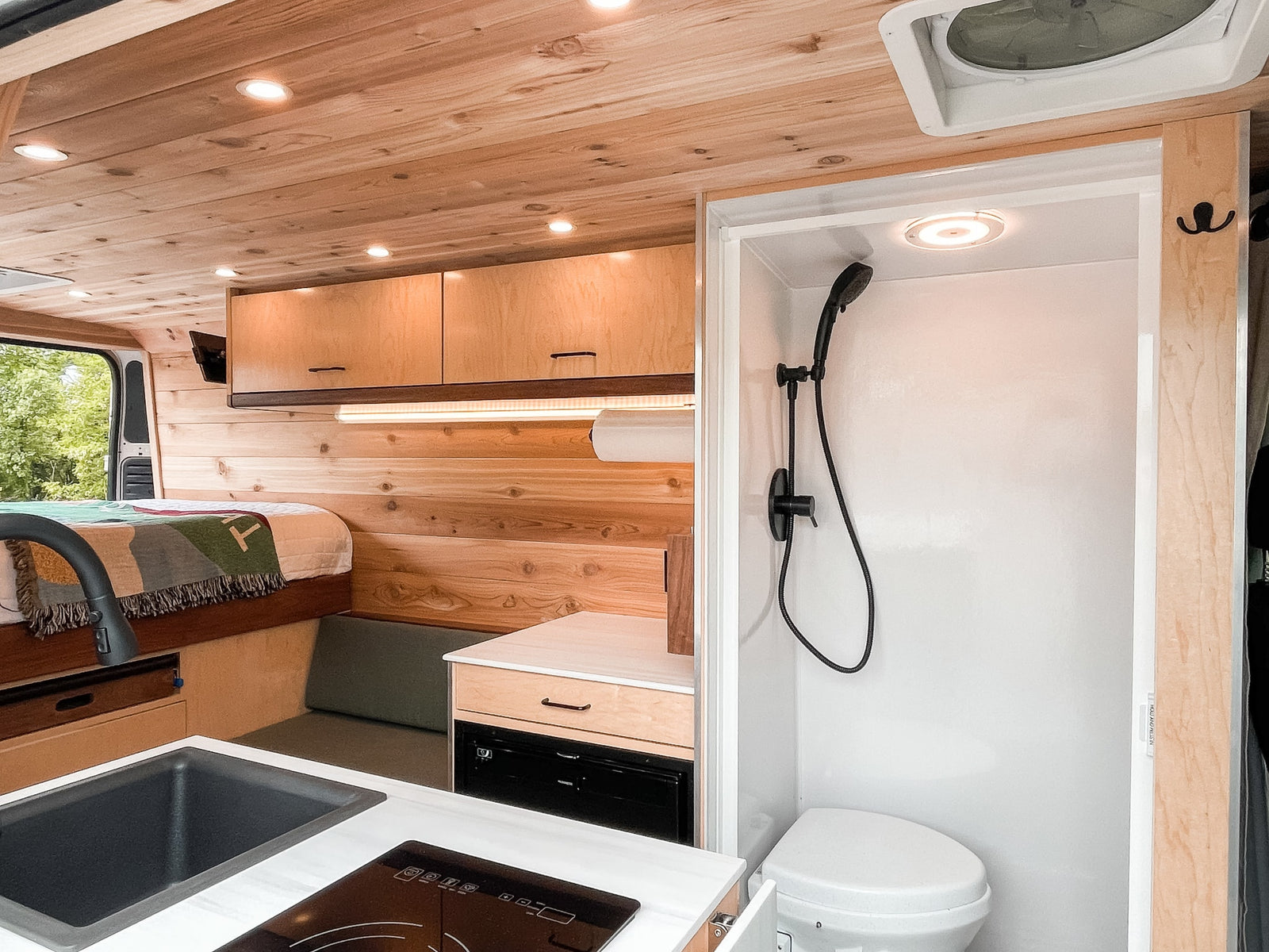 custom wooden interior.|Interior of an RV rental: a wooden-paneled campervan featuring a bed