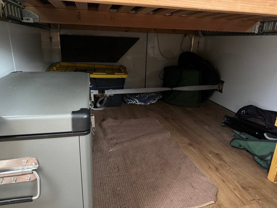 RV rental under-bed storage features a secured portable fridge, bins, and camping gear with a tie-down strap.