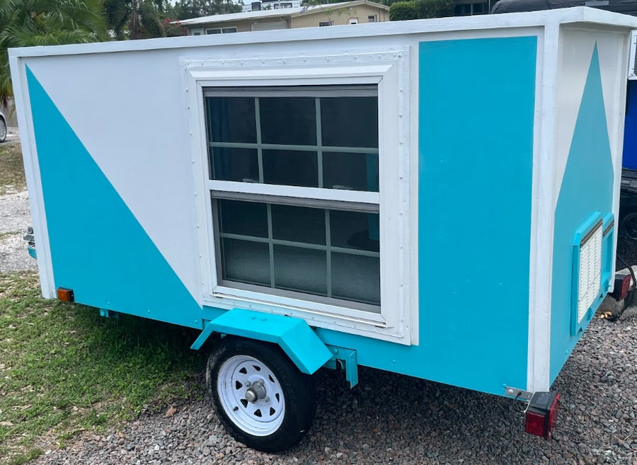 Teal & white RV rental trailer with a diagonal color design and a prominent side window.|This custom-built teal & white small trailer