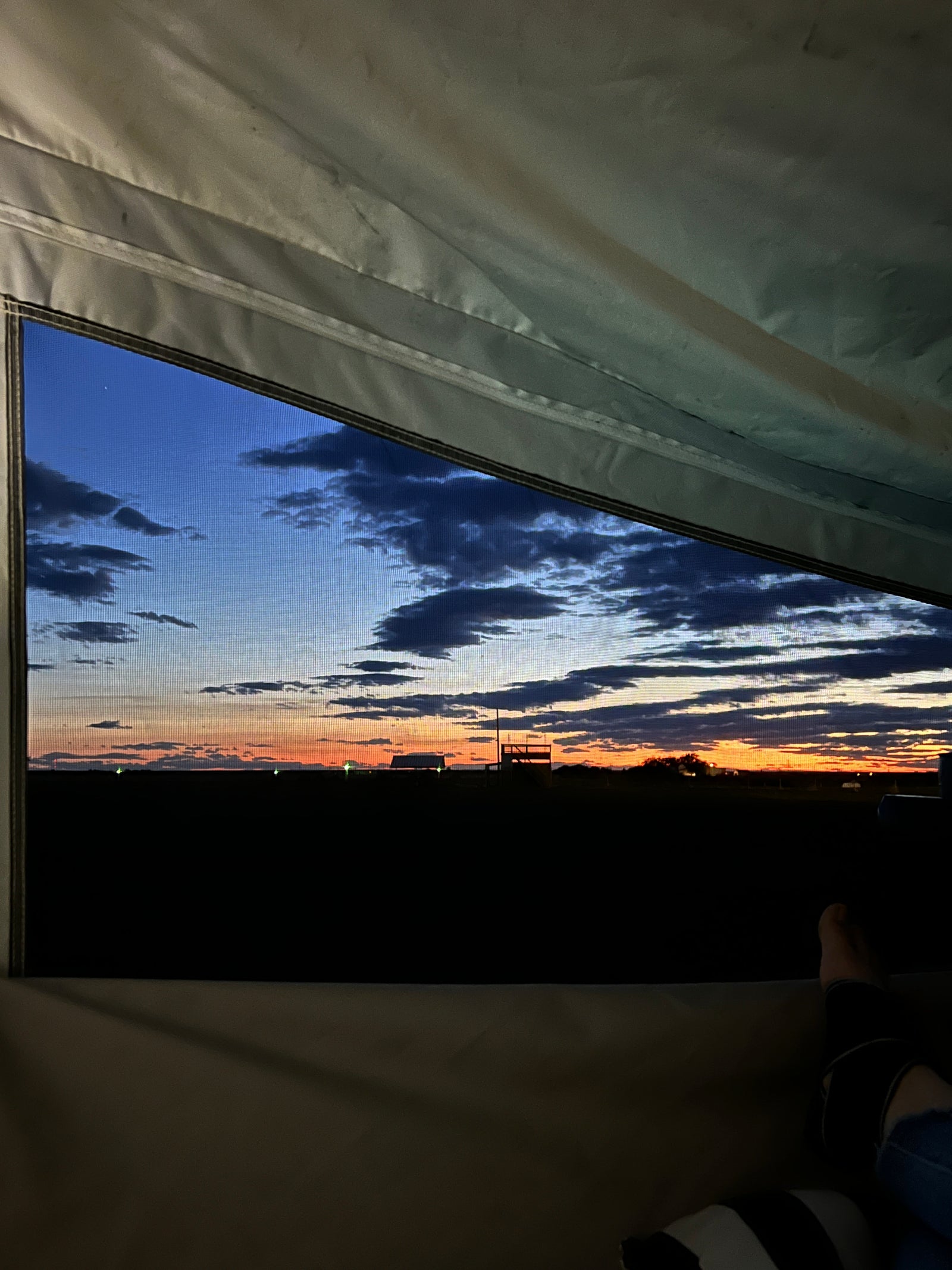Relaxing inside an RV rental, admiring a stunning sunset through the window screen, showcasing a vibrant sky & distant horizon.