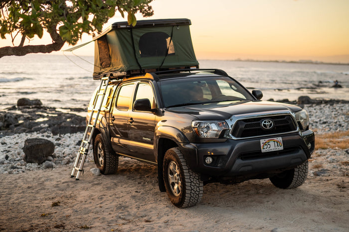 more versatile than a typical RV rental.|Adventure-ready RV rental truck perched on a rugged cliff overlooking the blue ocean. Ideal for exploring scenic coastal landscapes.|Coastal RV rental truck with rooftop tent and camp setup