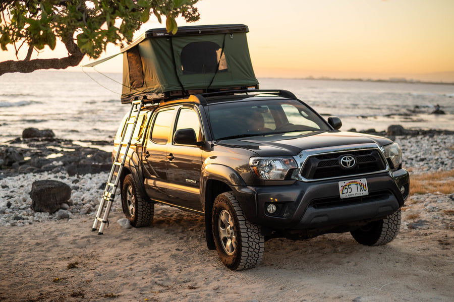 Experience RV rental adventure: A Tacoma truck with rooftop tent ready for beachside camping in Hawaii at sunset.