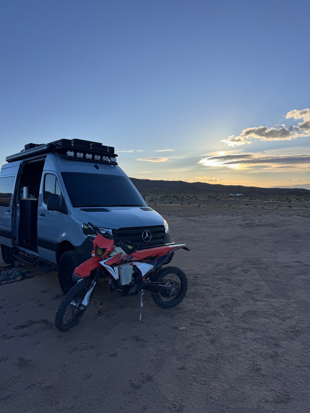 Experience van life! An RV rental van and dirt bike parked in a vast desert landscape at sunset, ready for adventure. — photo 2