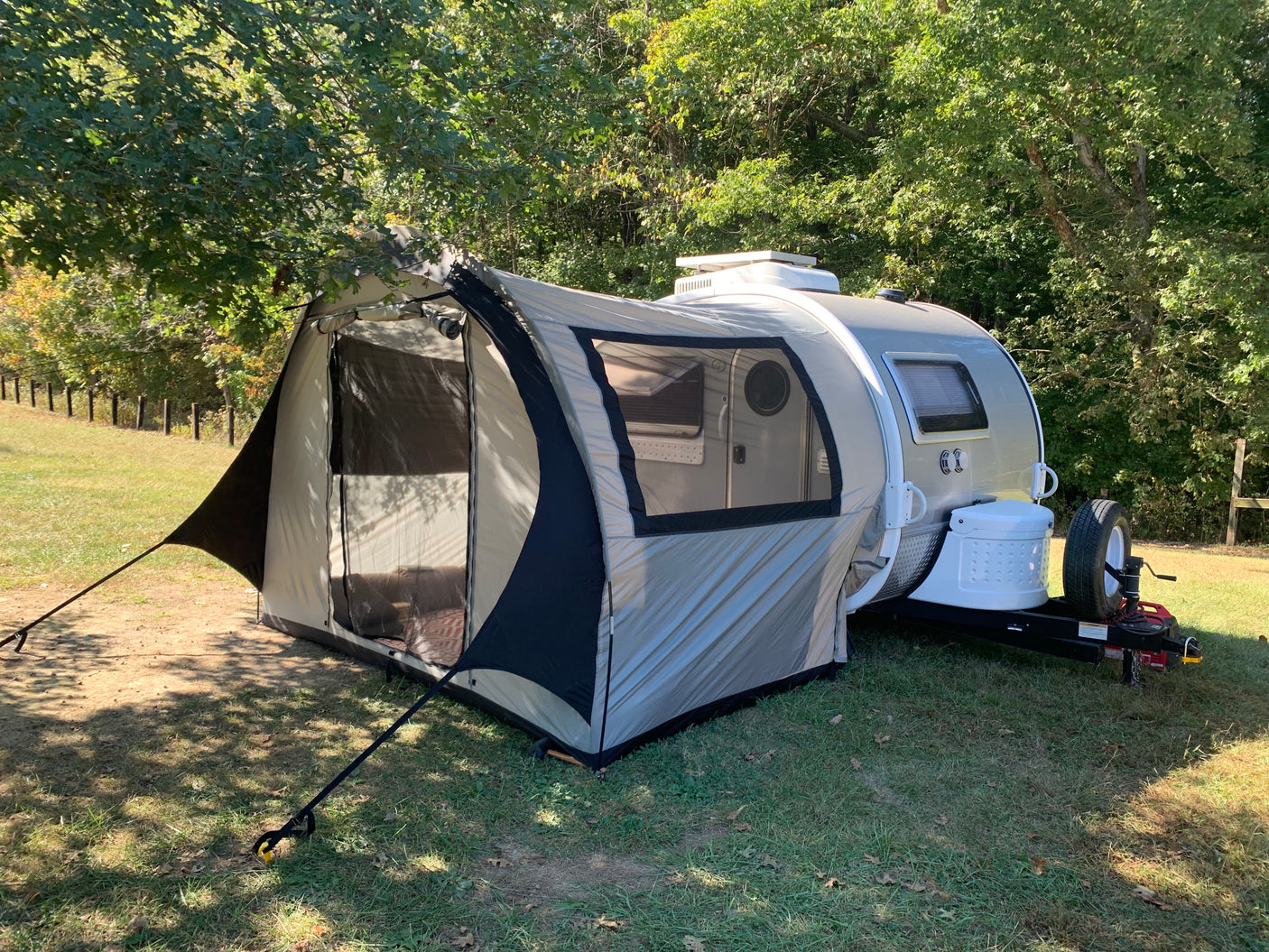 This rv rental setup features a teardrop trailer with an attached tent, perfect for camping in nature.