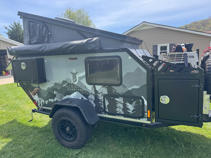 This rugged Mission Overland trailer, featuring mountain graphics, pop-up tent, and off-road tires, is ideal for your next RV rental adventure or off-road camping trip.