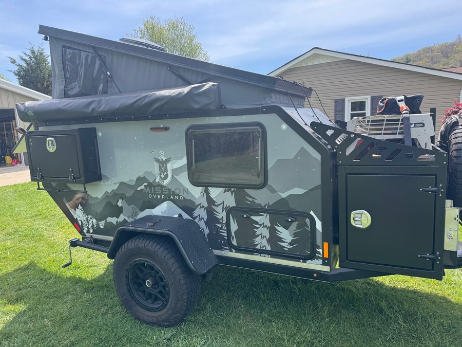 This rugged Mission Overland trailer, featuring mountain graphics, pop-up tent, and off-road tires, is ideal for your next RV rental adventure or off-road camping trip.