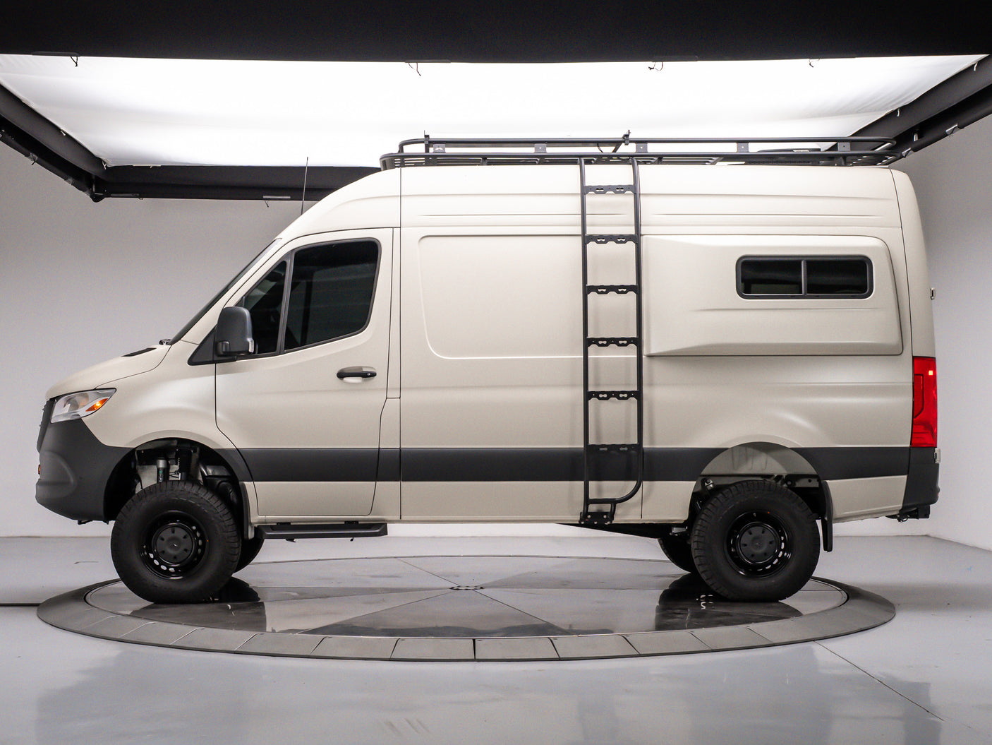 Side view of a tan Mercedes Sprinter rv rental camper van with a roof rack and ladder, on a studio turntable.