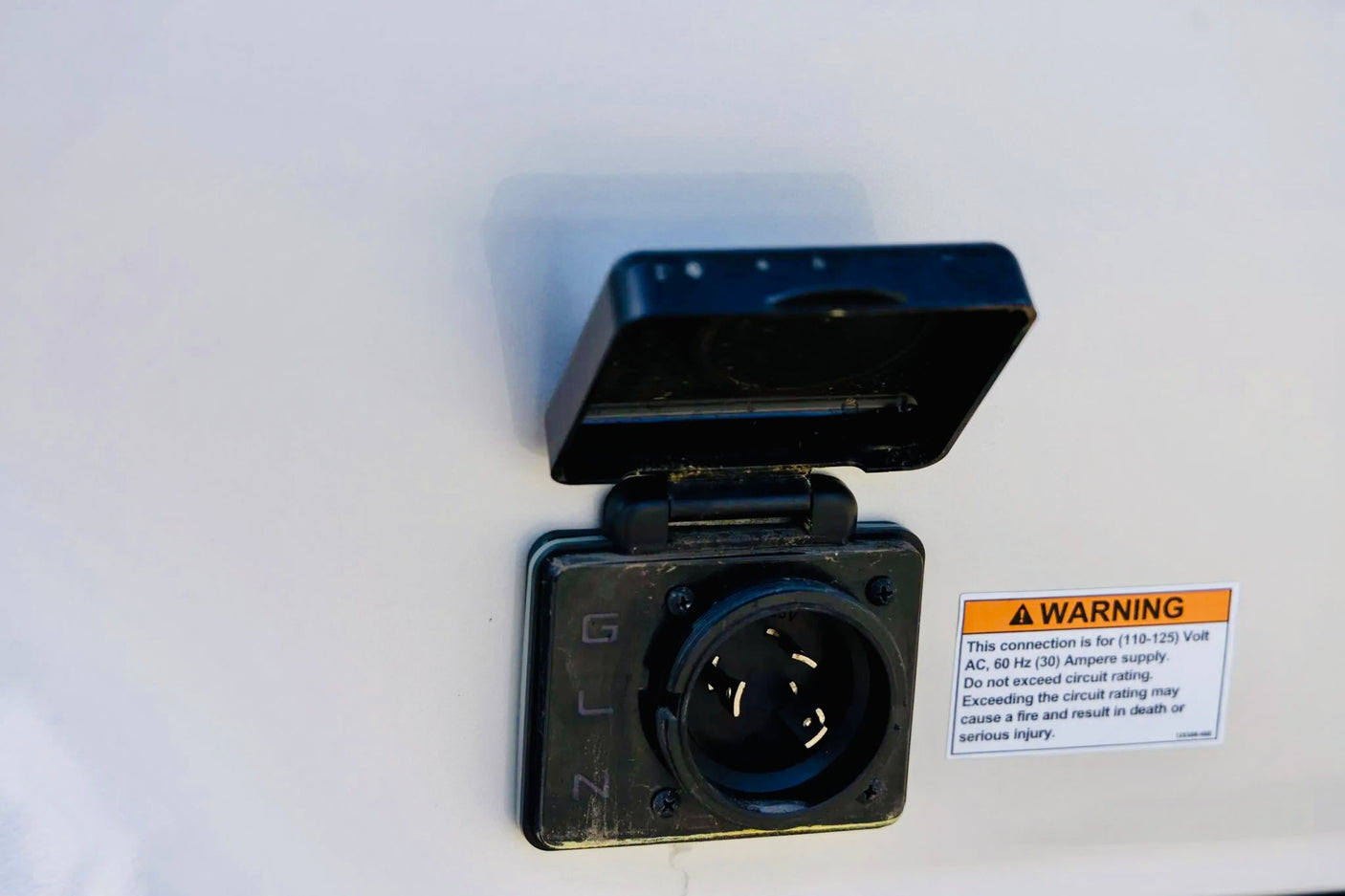 RV rental's 30 amp electrical shore power inlet with open cover and warning label. Essential for safe RV power connection.