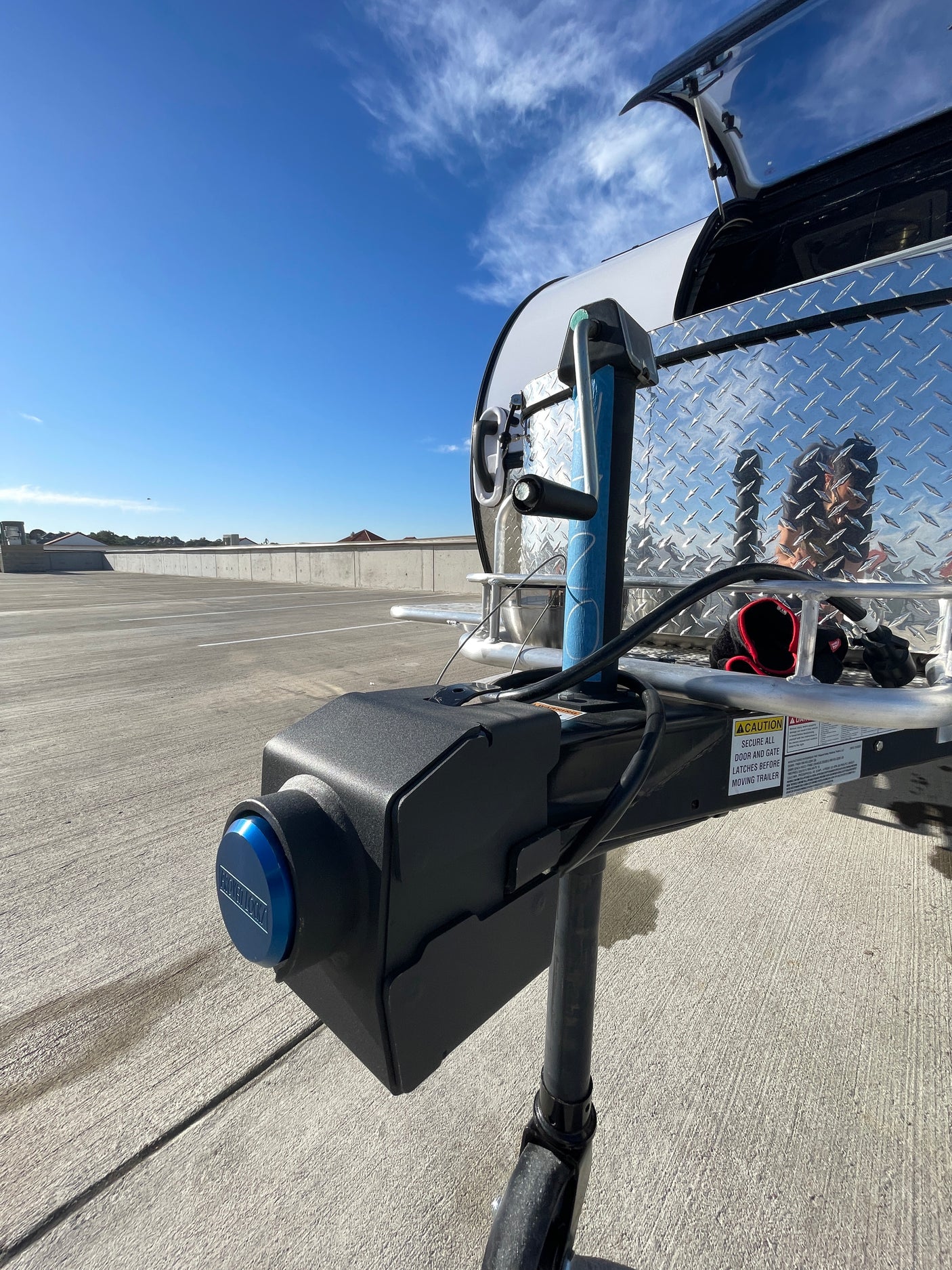 Front view of an RV rental trailer's hitch with a blue locking mechanism and warning label, parked on a concrete lot under a blue sky.