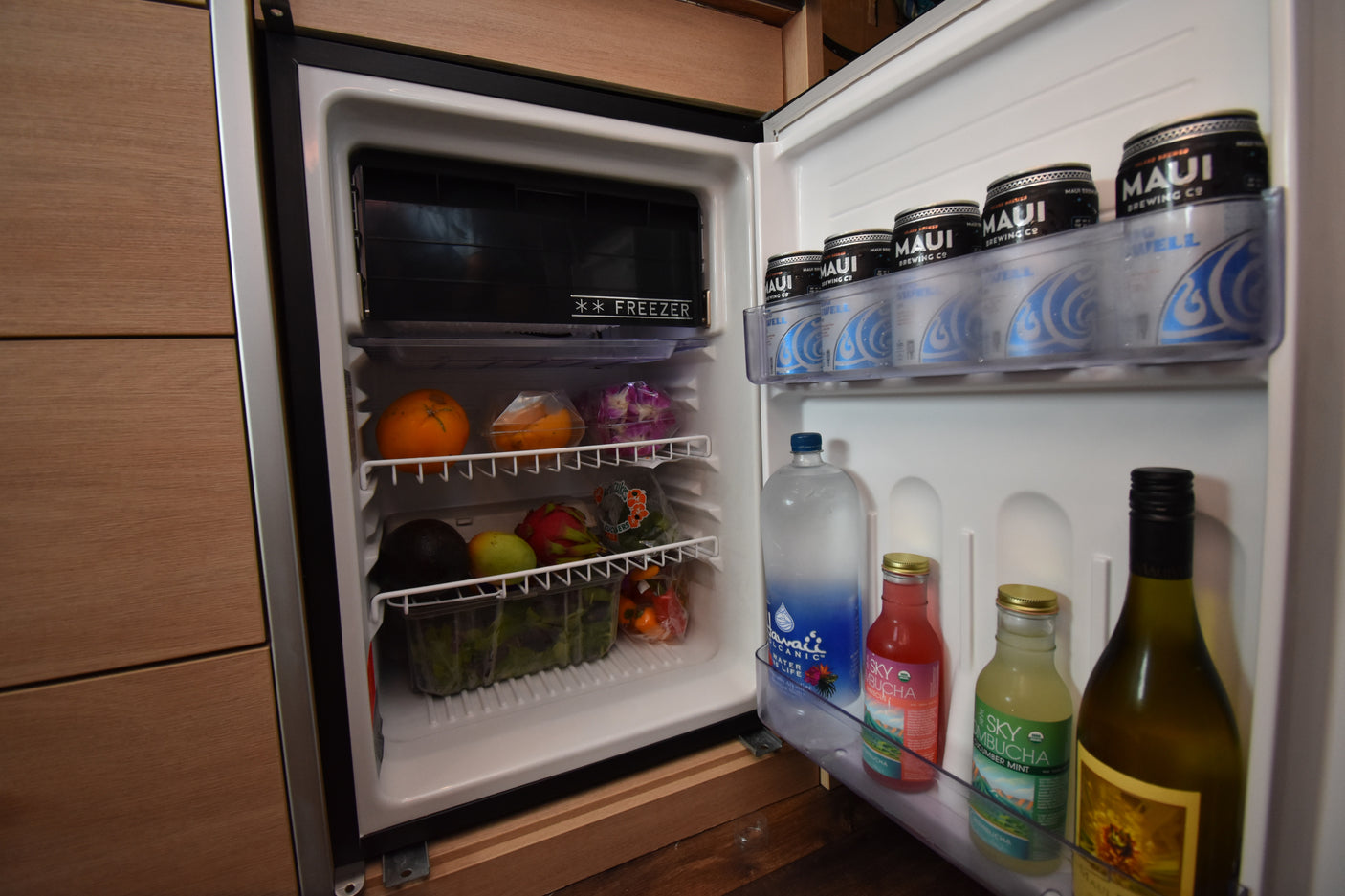 RV rental mini-fridge stocked with Maui beer, kombucha, water, fresh fruits (oranges, dragon fruit), and veggies.