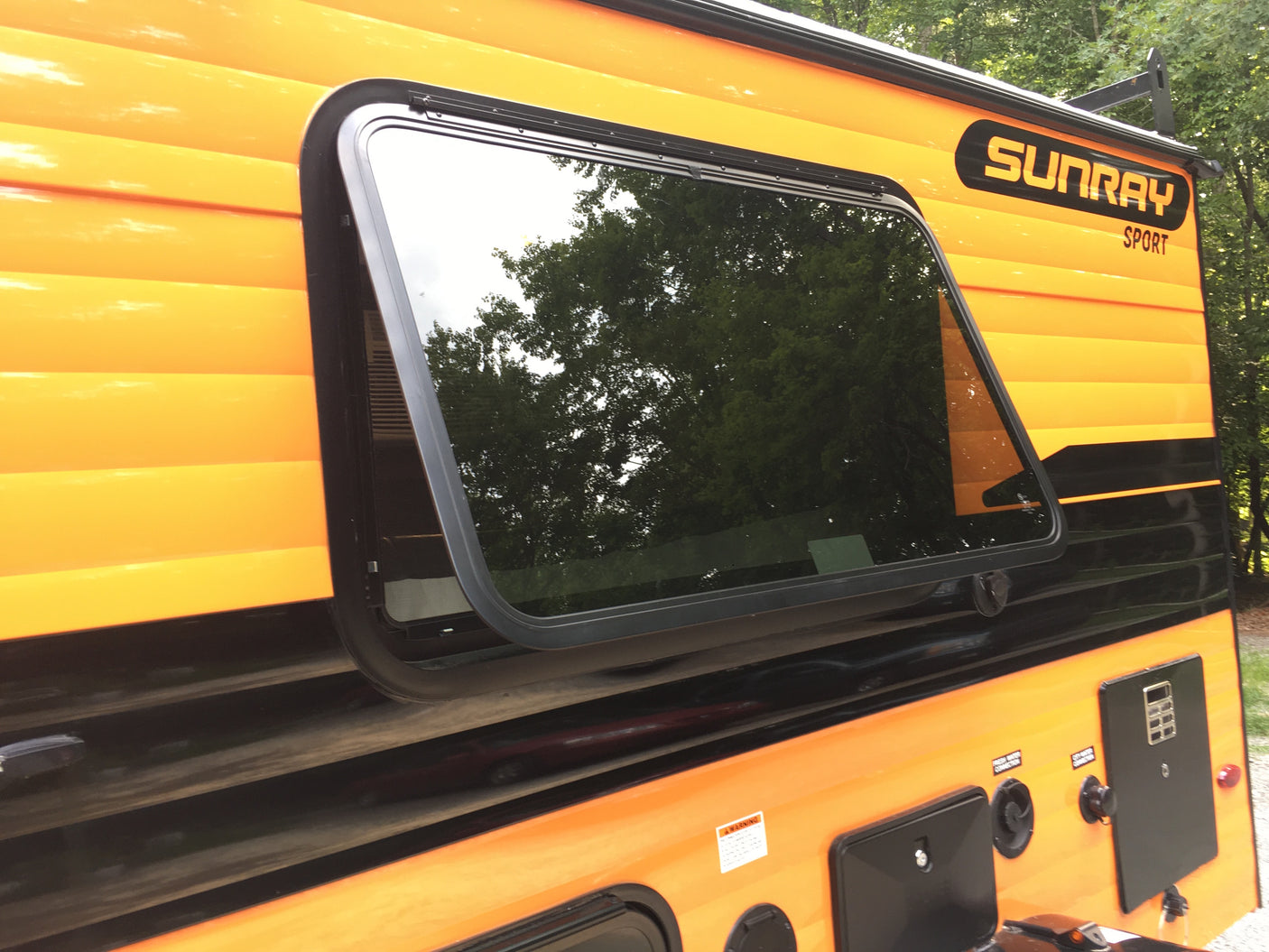 Orange & black Sunray Sport RV rental, a travel trailer with large window & utility hookups.