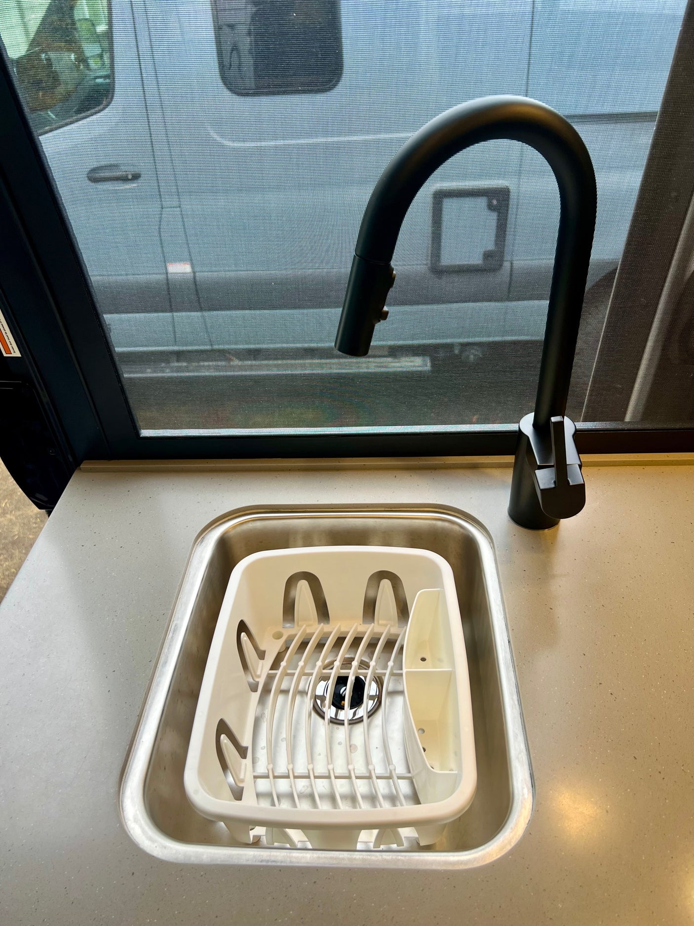 Close-up of an RV rental kitchen sink with a white dish rack, modern black faucet, and screened window view.