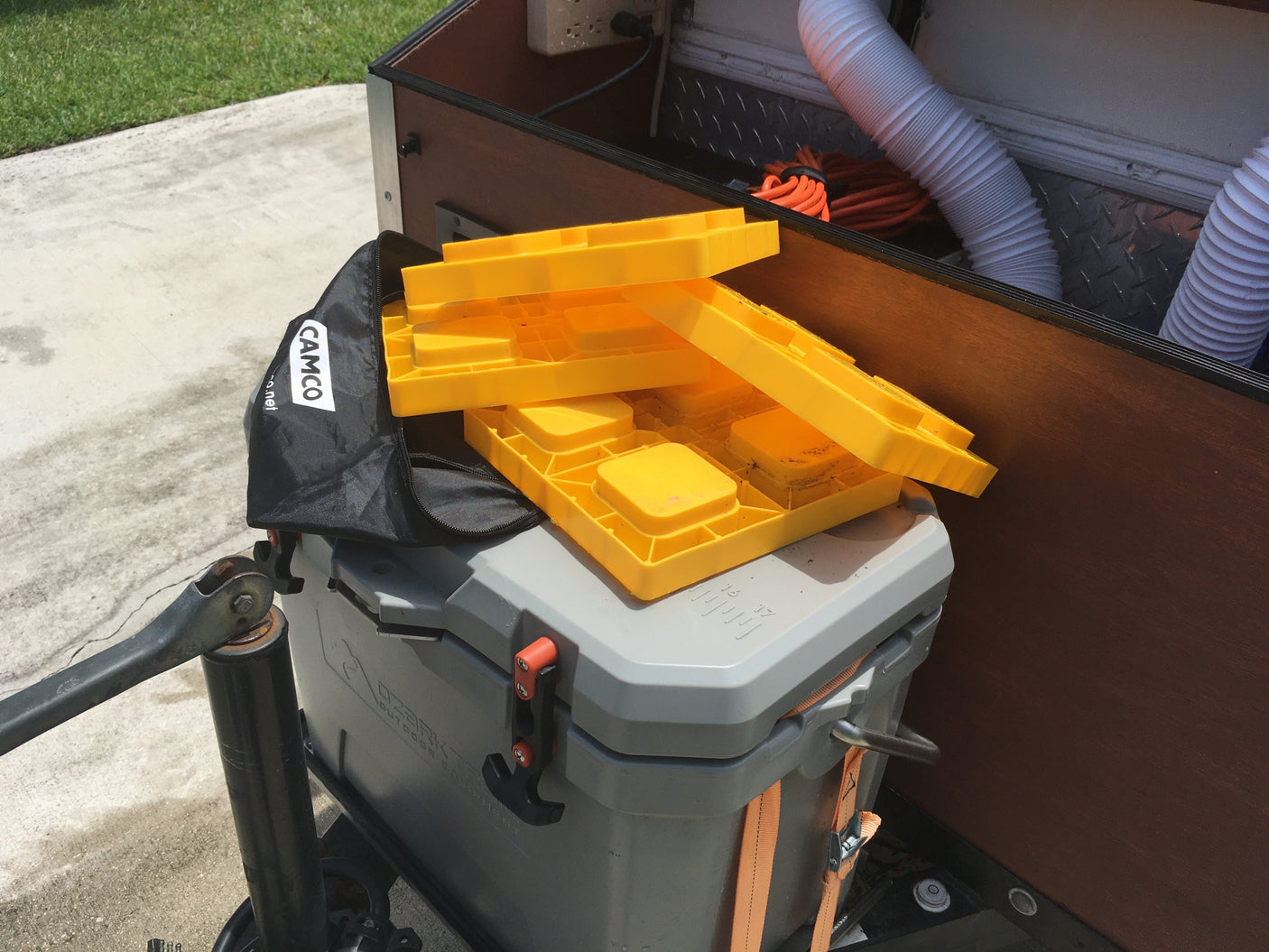 Essential RV rental gear: yellow Camco leveling blocks, a grey cooler, and camping supplies stored in the trailer.