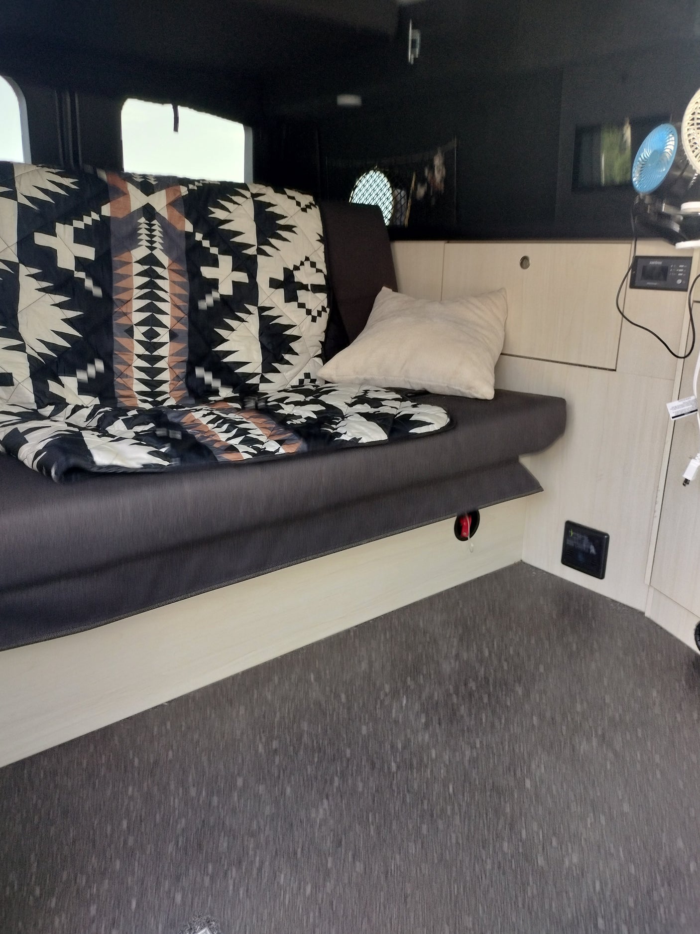 Cozy RV rental interior with patterned blanket, pillow, and portable fans. Ideal for travel.