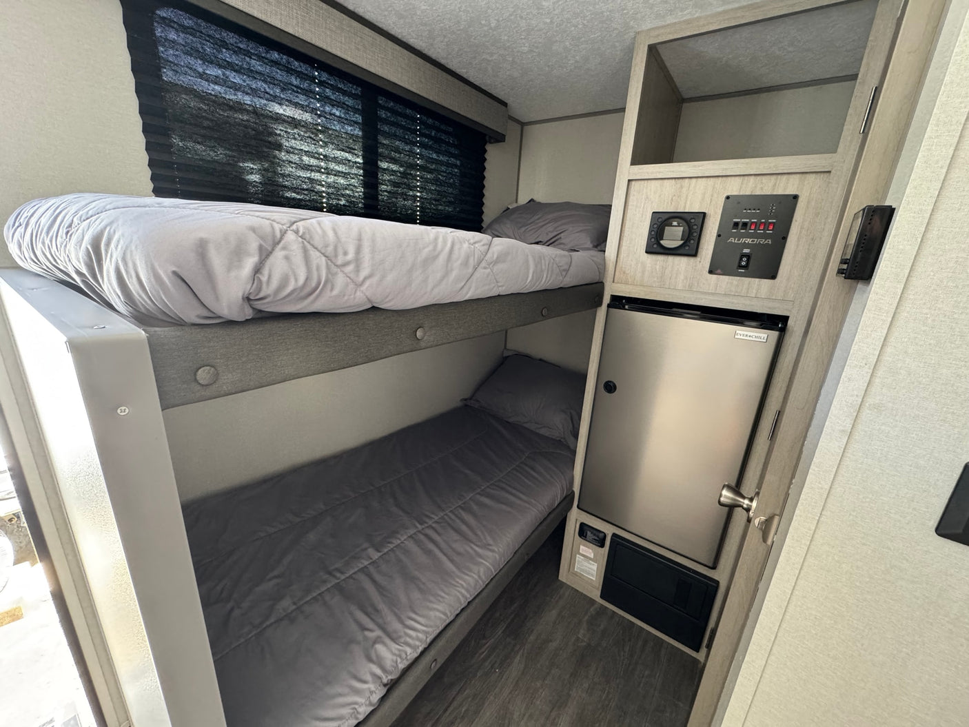 Inside this RV rental: comfortable bunk beds with grey bedding, a mini-fridge, and control panels. Ideal for family travel.