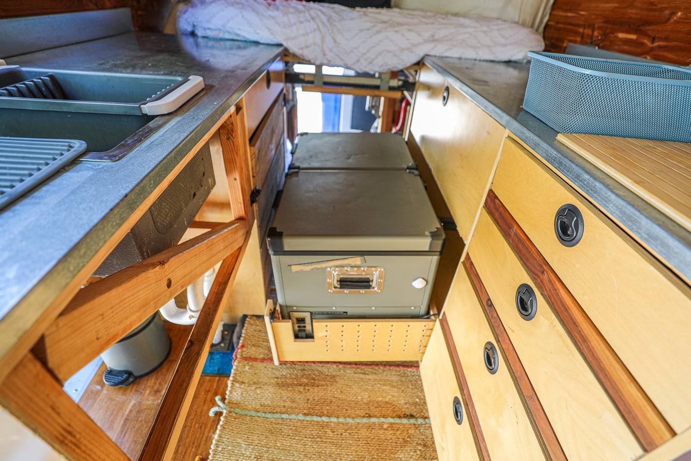 Compact RV rental interior with kitchen sink, bed, and a central pull-out fridge for convenient travel.