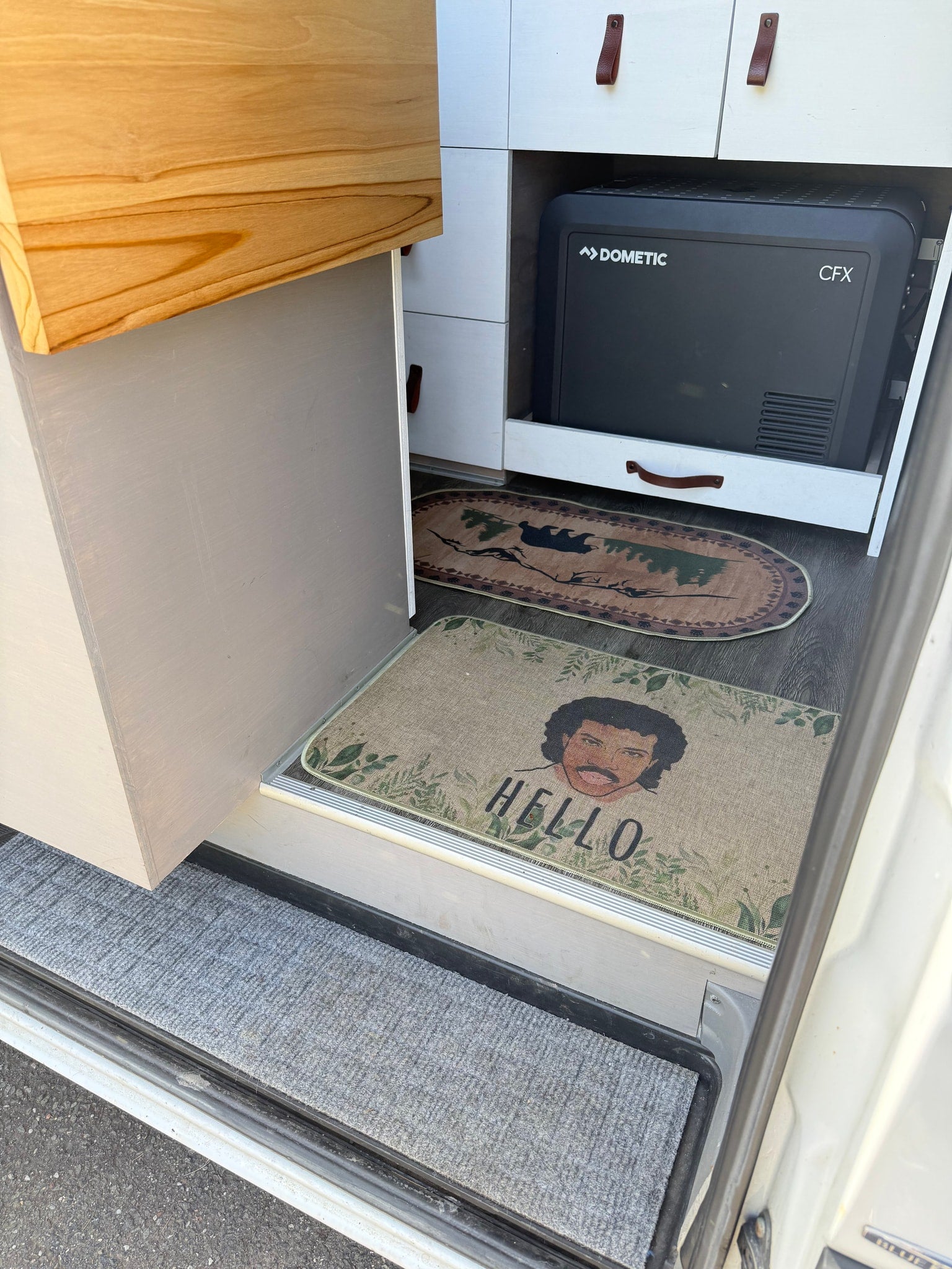 Inside this unique RV rental: custom woodwork, a Dometic fridge, and a fun Lionel Richie "HELLO" mat at the entrance.