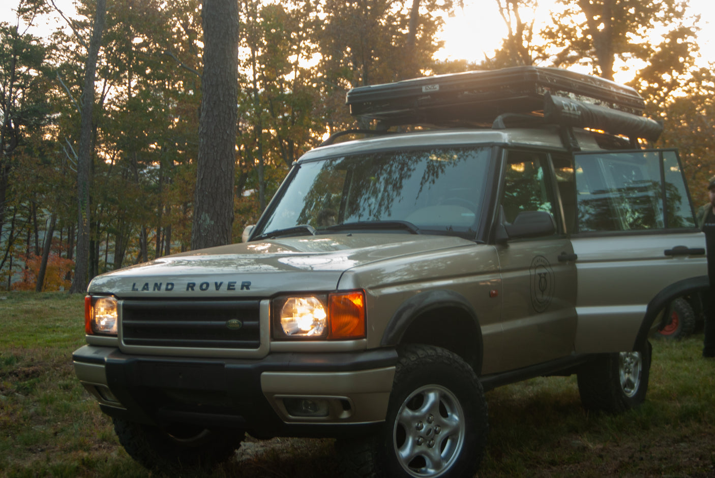 Golden light illuminates a Land Rover Discovery SUV with a roof tent, an ideal RV rental for scenic outdoor adventures.