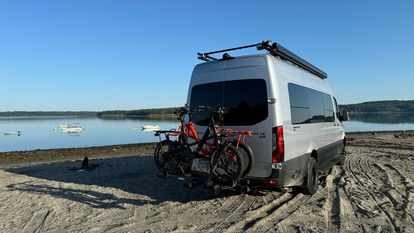 backed onto a sandy beach by a tranquil bay.|Stunning pink sunset and faint rainbow over an RV rental parked on a wet road