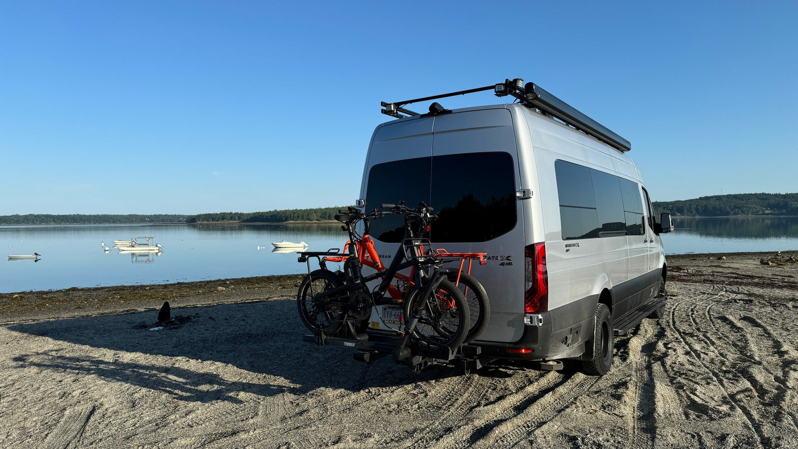 backed onto a sandy beach by a tranquil bay.|Stunning pink sunset and faint rainbow over an RV rental parked on a wet road
